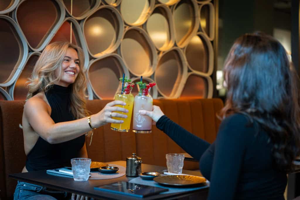 Zwei Frauen stoßen mit Mojitos in einem modernen Restaurant in Salzburg an.