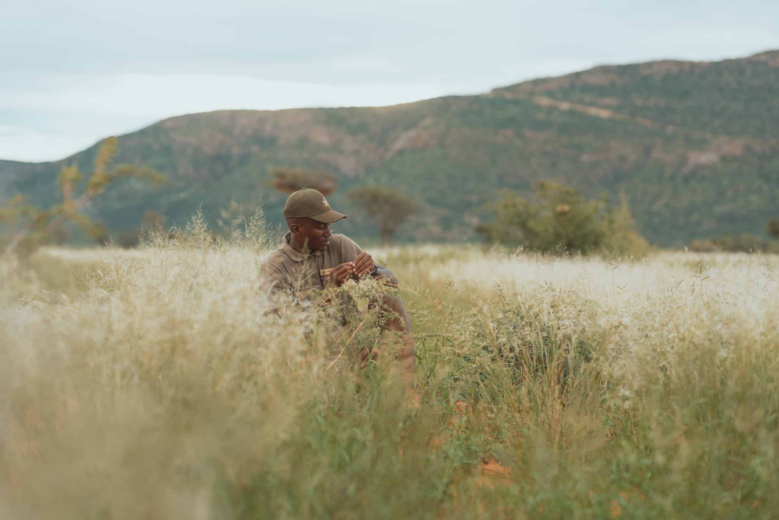 Mann sitzt in der Natur bei Gmundner Lodge Namibia, umgeben von Gras und Bergen.
